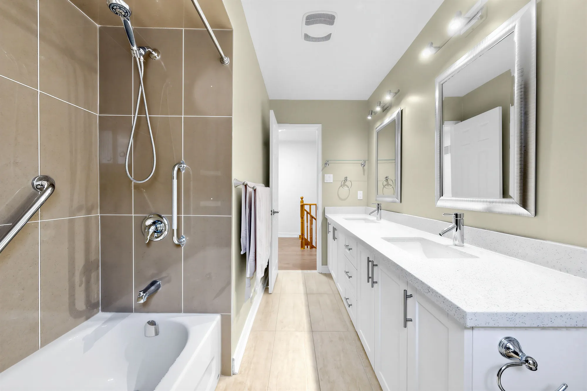 The bathroom: a tub with a tiled surround and grab bars, a long white double vanity with a quartz top, two mirrors, a light bar