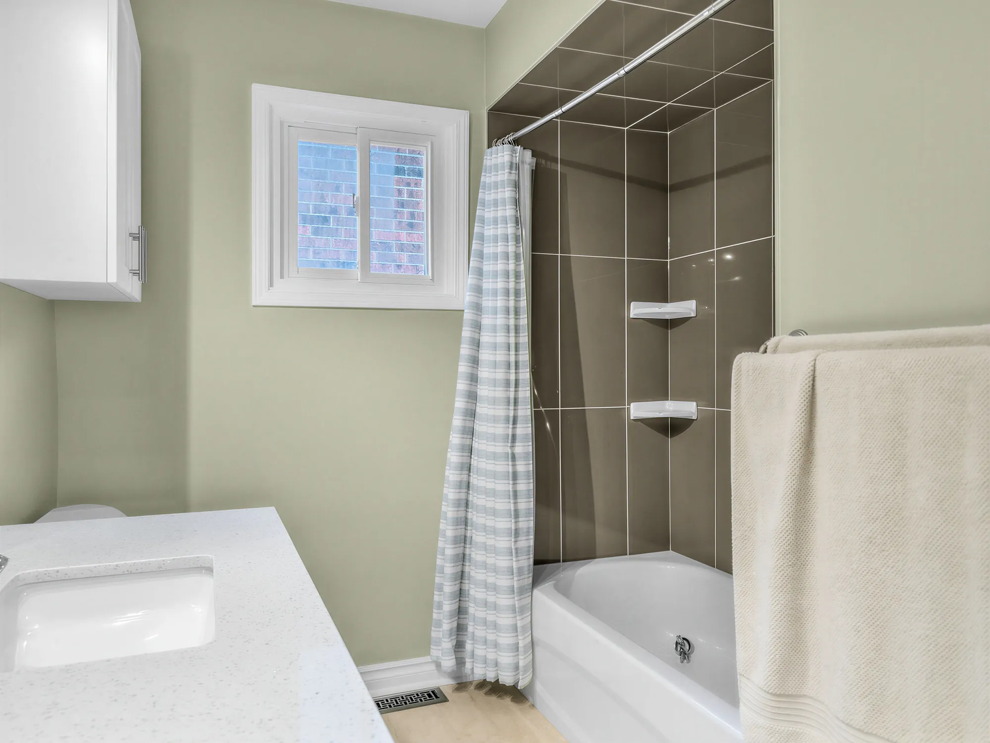 The tub with a curtain, a dark tiled surround and corner shelves, a window, a towel bar