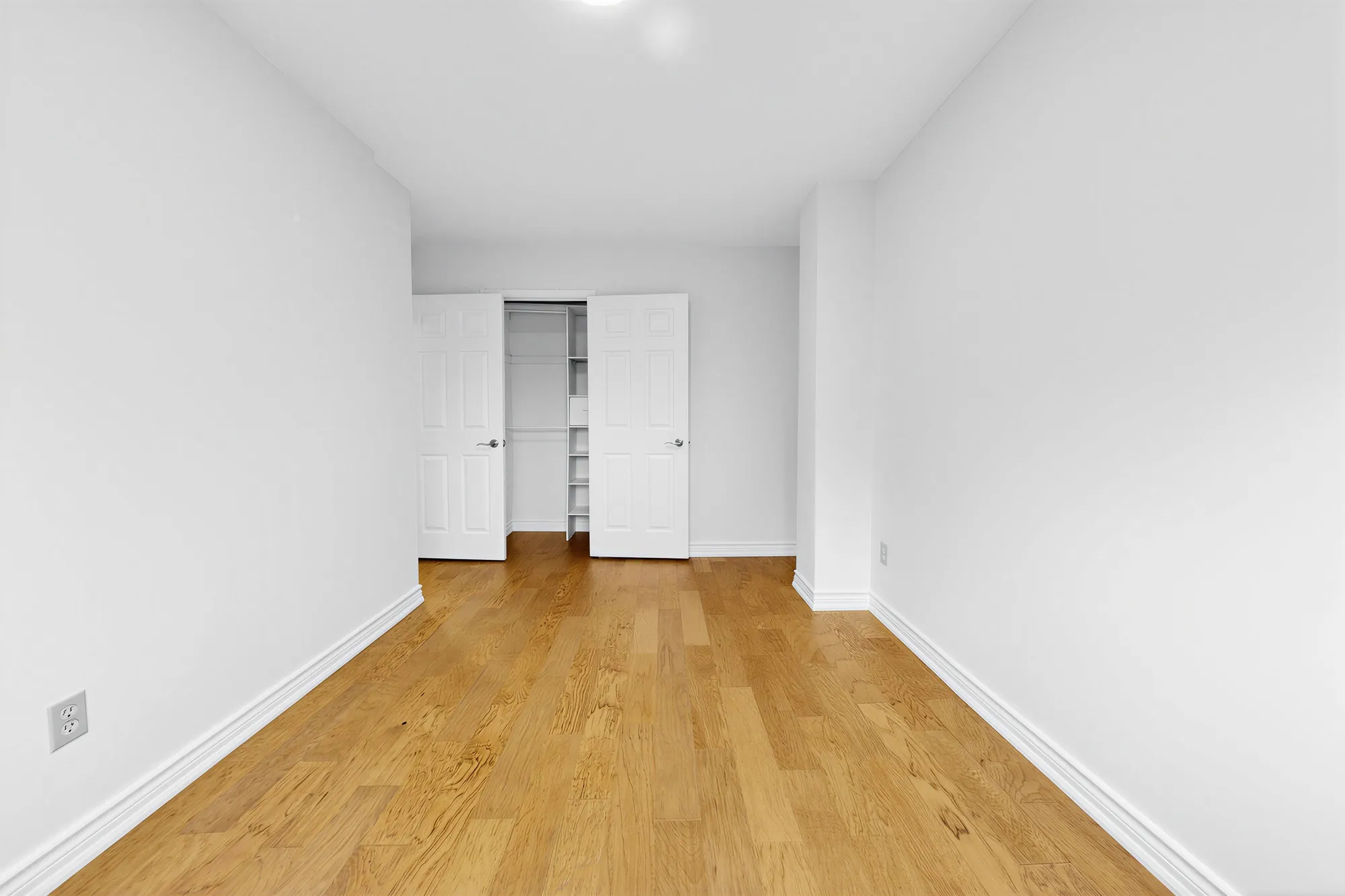 The same bedroom toward its closet with the doors open and shelves inside