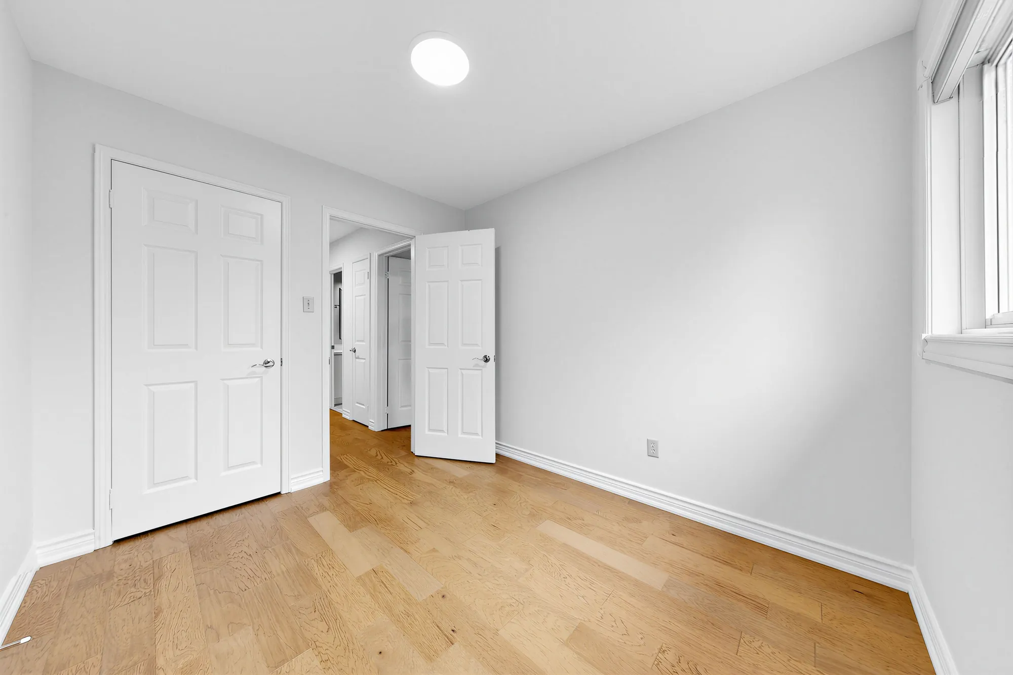 The same bedroom toward its door and the closet, the hall beyond, a window at the right