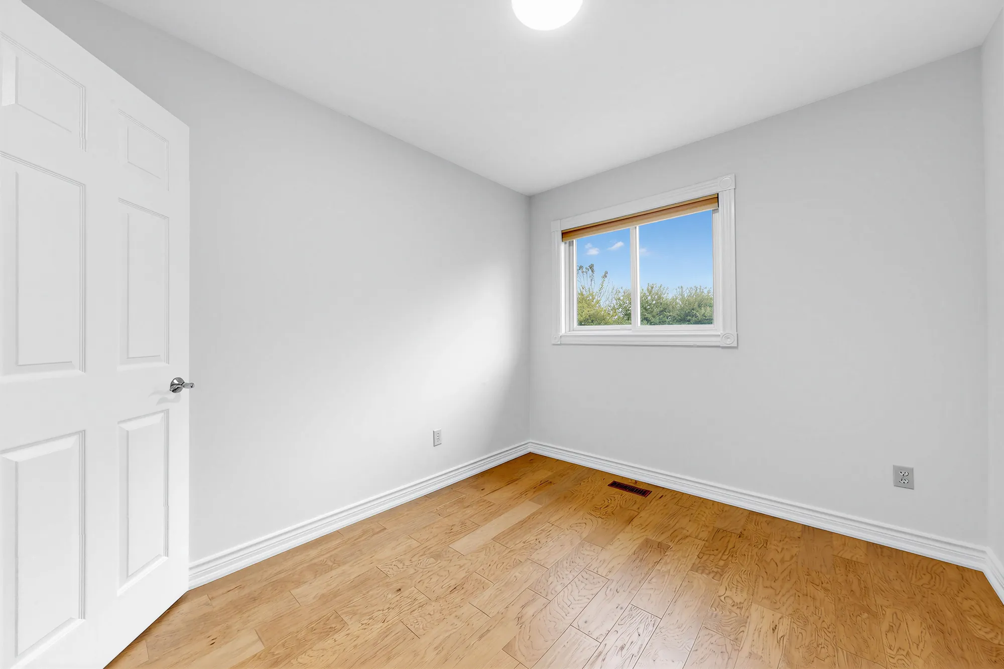 The same bedroom toward its window, the door at the left