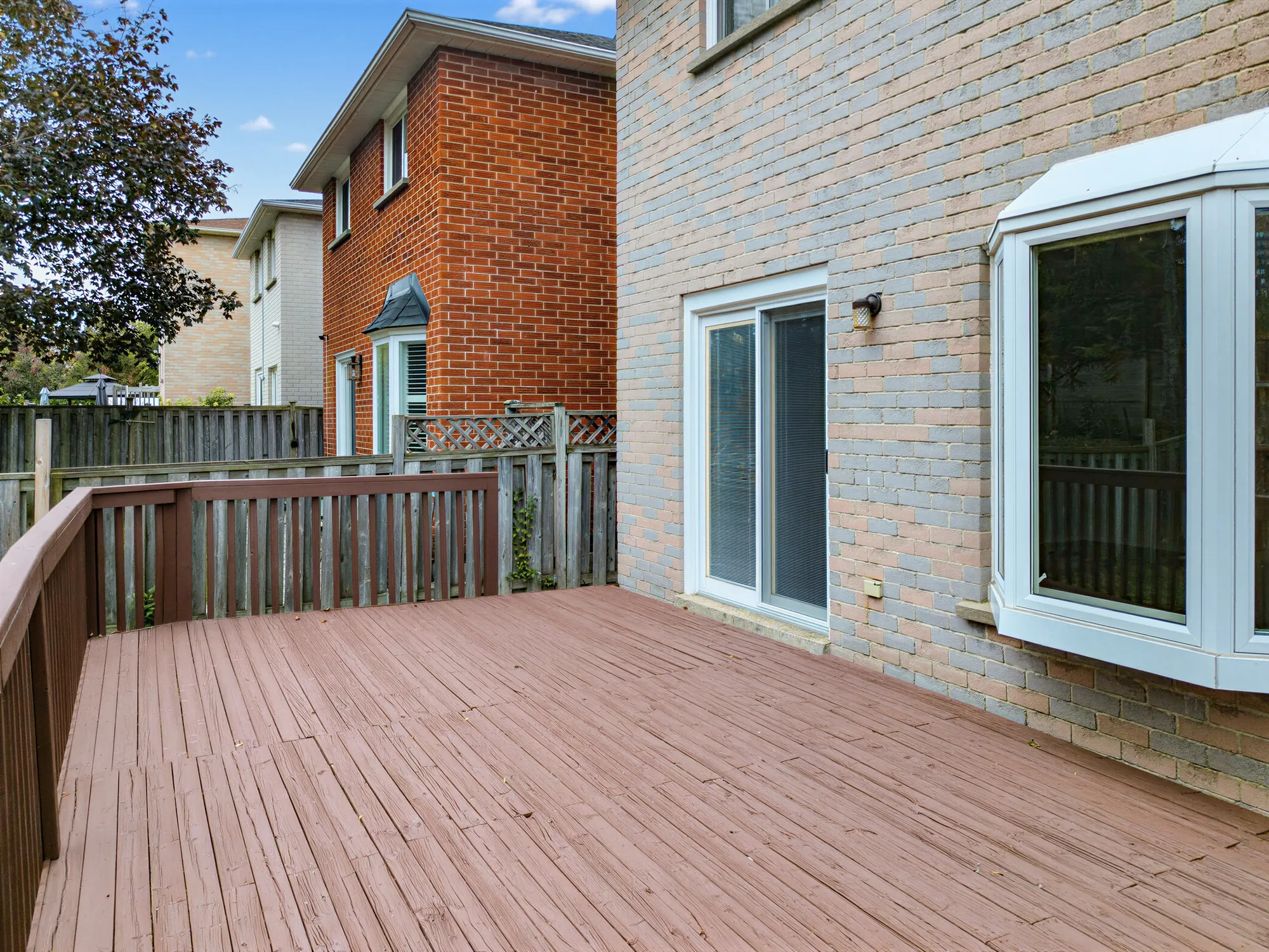 The deck toward the back of the house: a sliding door and a bay window opening onto it, the railing, a neighbouring house