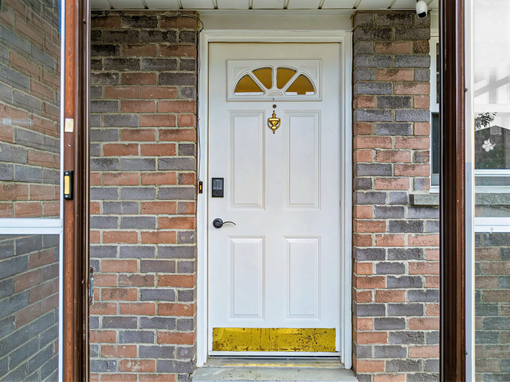 The front door inside the enclosed porch: a white door with an arched window and a keypad lock, brick walls on either side
