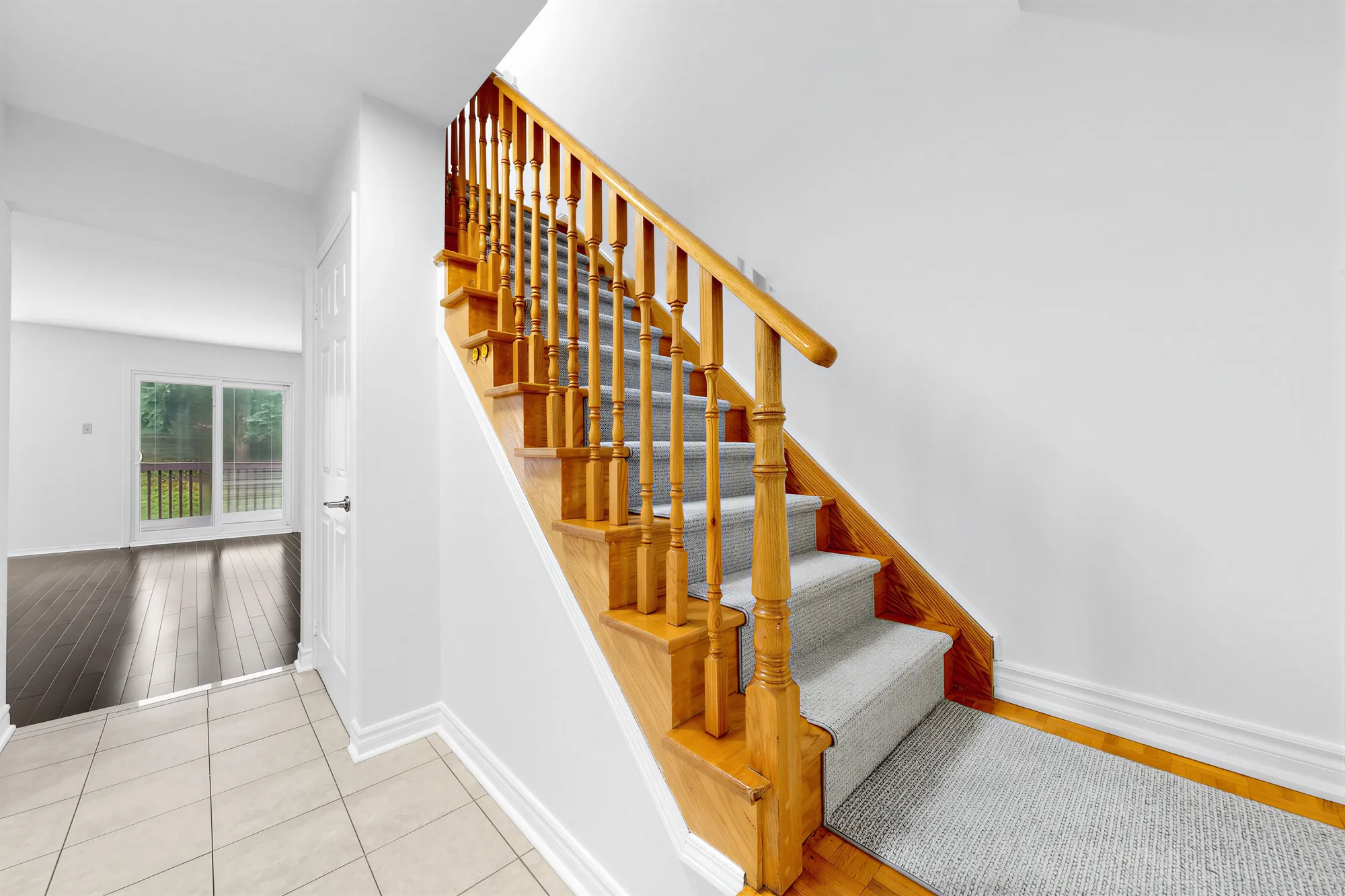 The front hall: the oak staircase with a carpet runner at the right, a tiled floor, the living room with its sliding door beyond