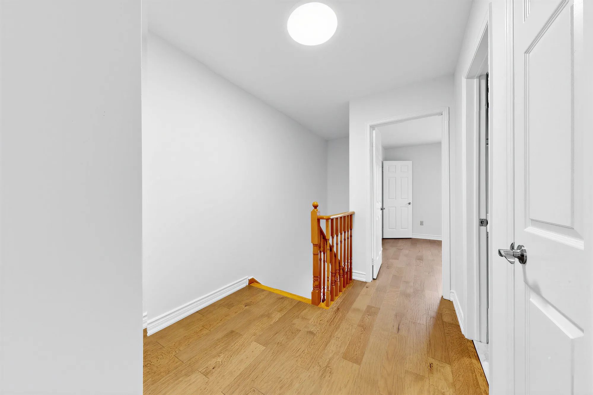 The upper hall: the top of the oak staircase, white doors to the bedrooms and the bathroom, new hardwood floors