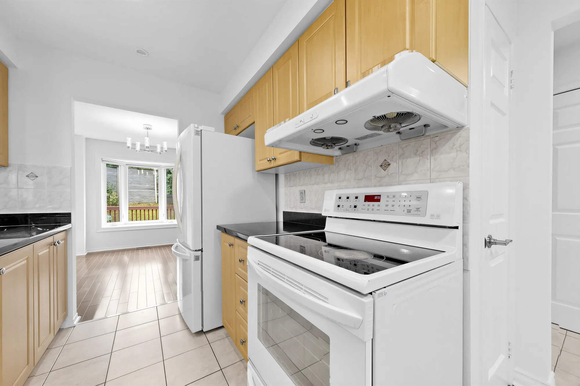 The white range under a hood fan, maple cabinets, a tiled backsplash, the fridge and the dining room beyond