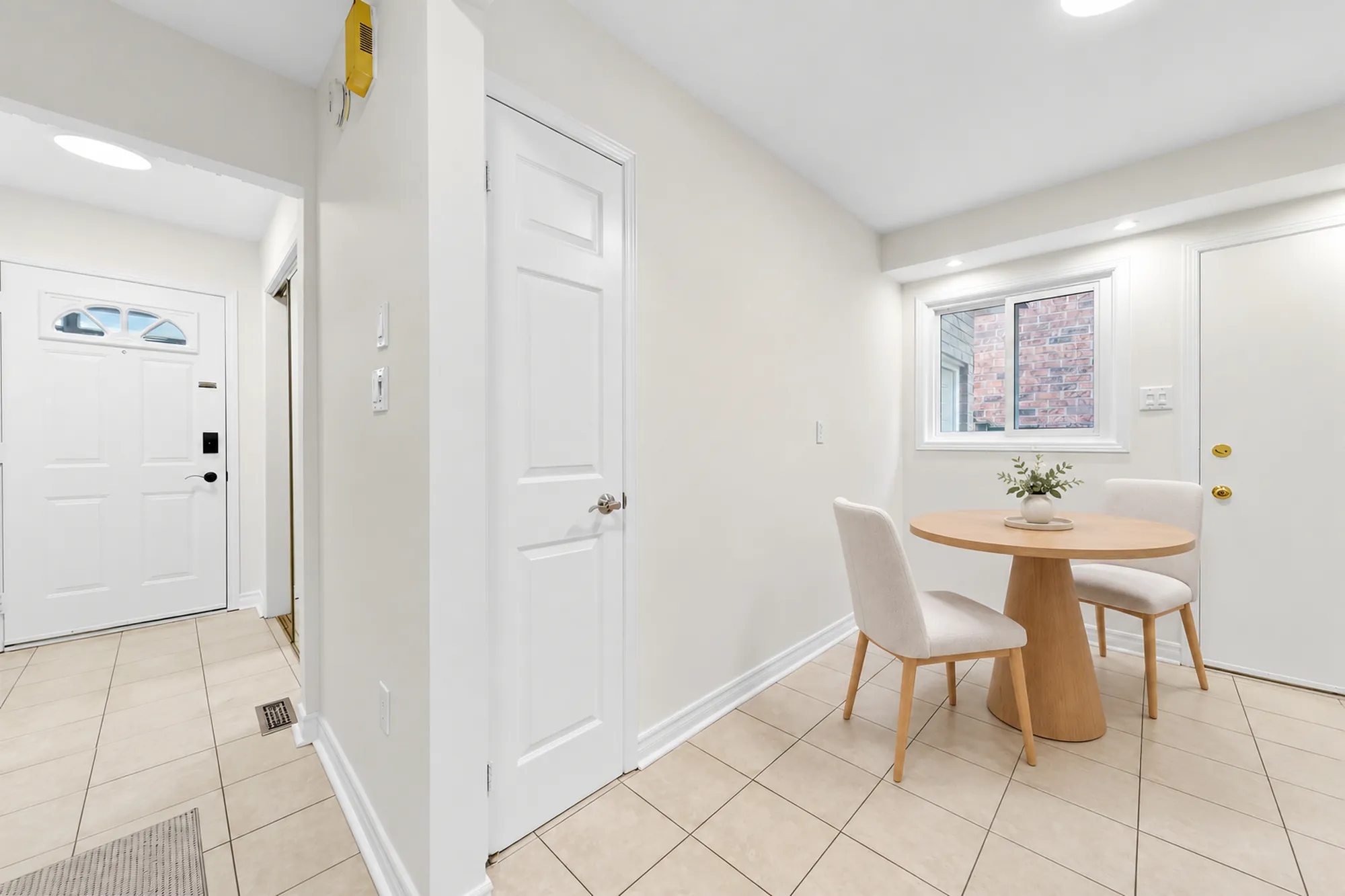 The breakfast nook, virtually staged: a round wood table and two upholstered chairs under a window, a door to the side, the front door down the hall