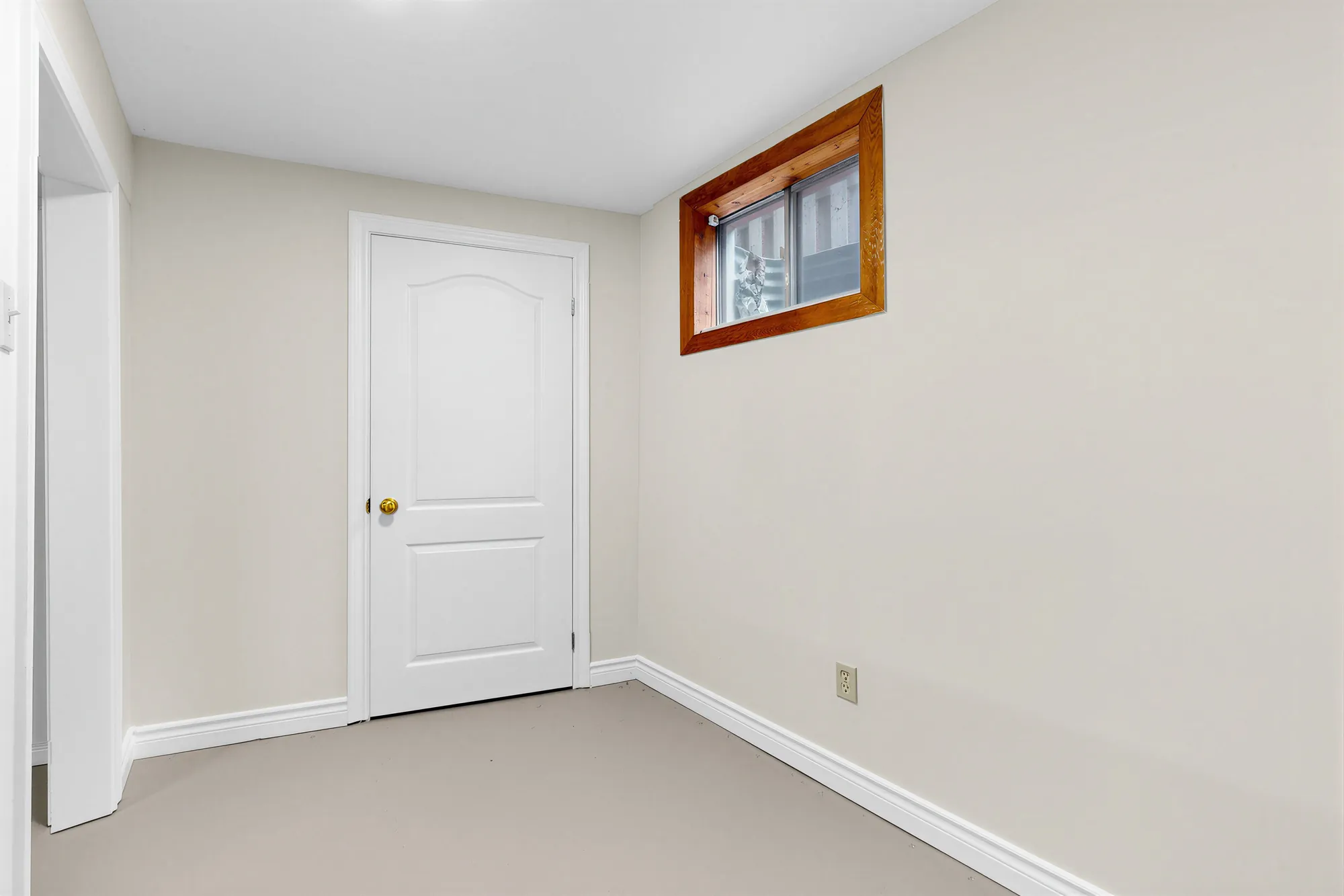 A small basement room: a white door, a window high in the wall, a painted floor