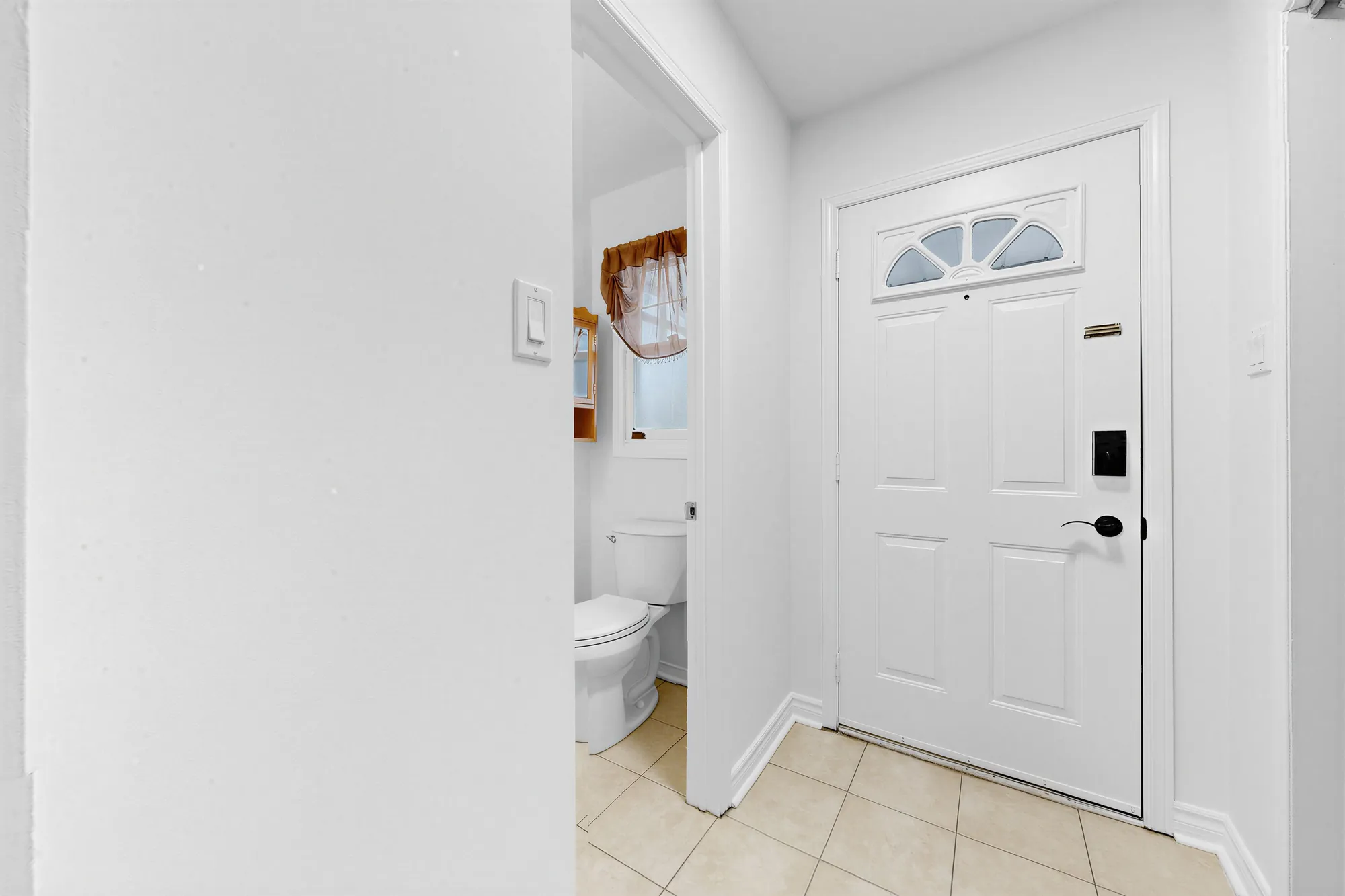 The front door from the hall, and through a door at the left the powder room with a toilet, a tiled floor