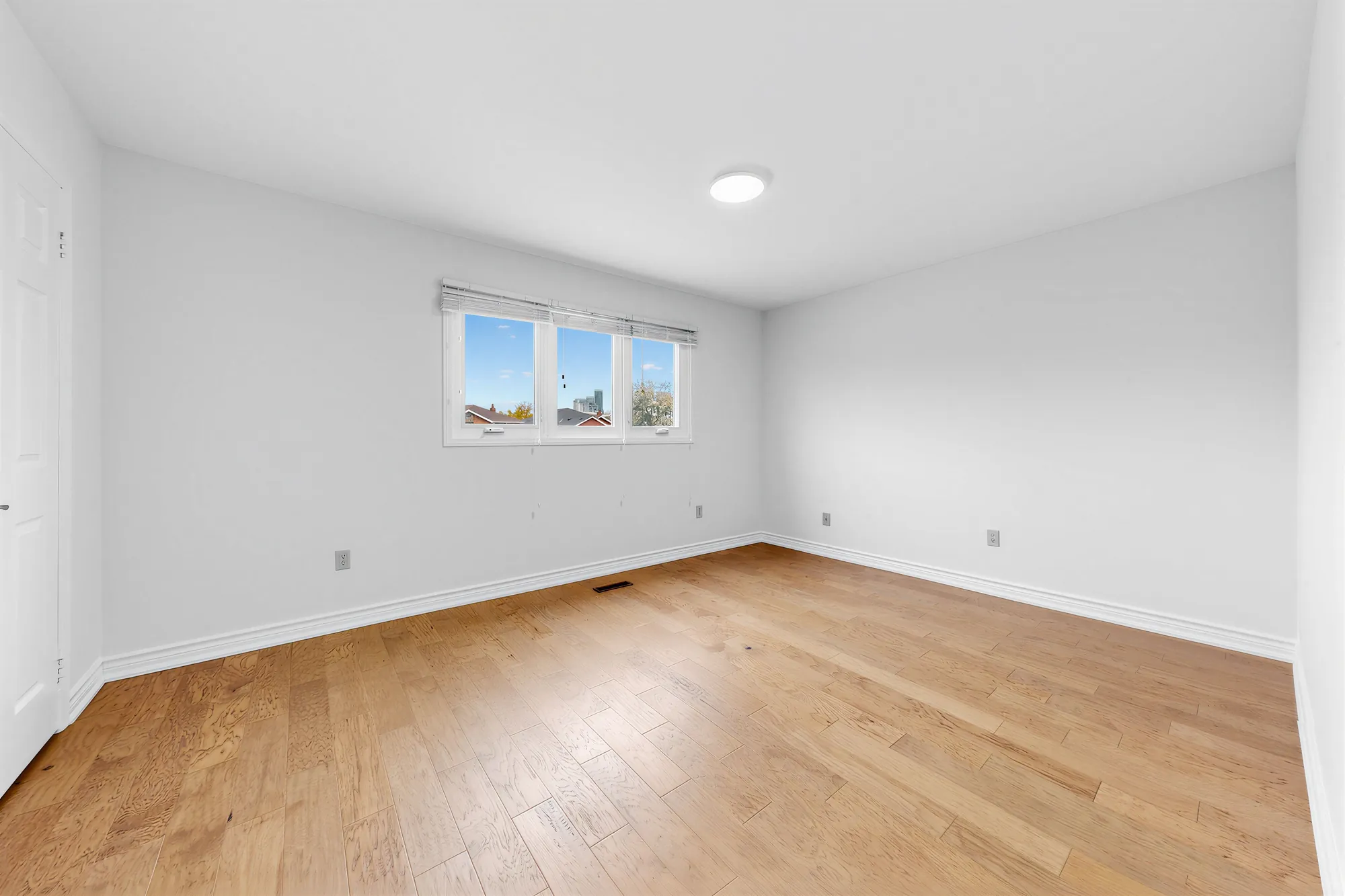 The primary bedroom, empty: a wide three-part window, hardwood floors, a ceiling light