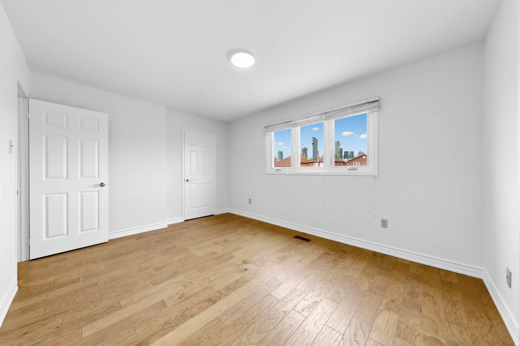 The primary bedroom toward its window and the closet doors, hardwood floors