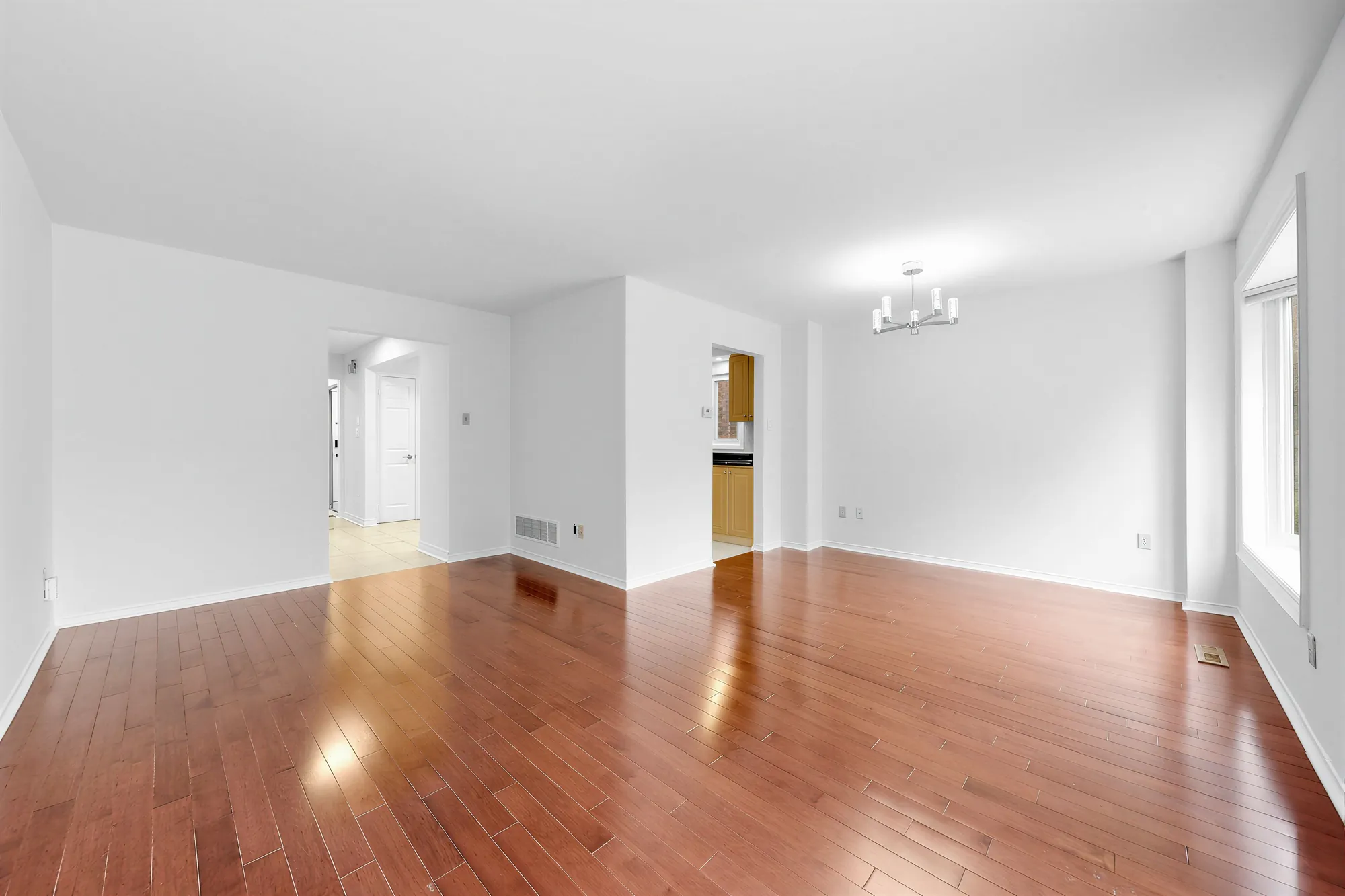 The living and dining room toward the doorways to the front hall and the kitchen, hardwood floors