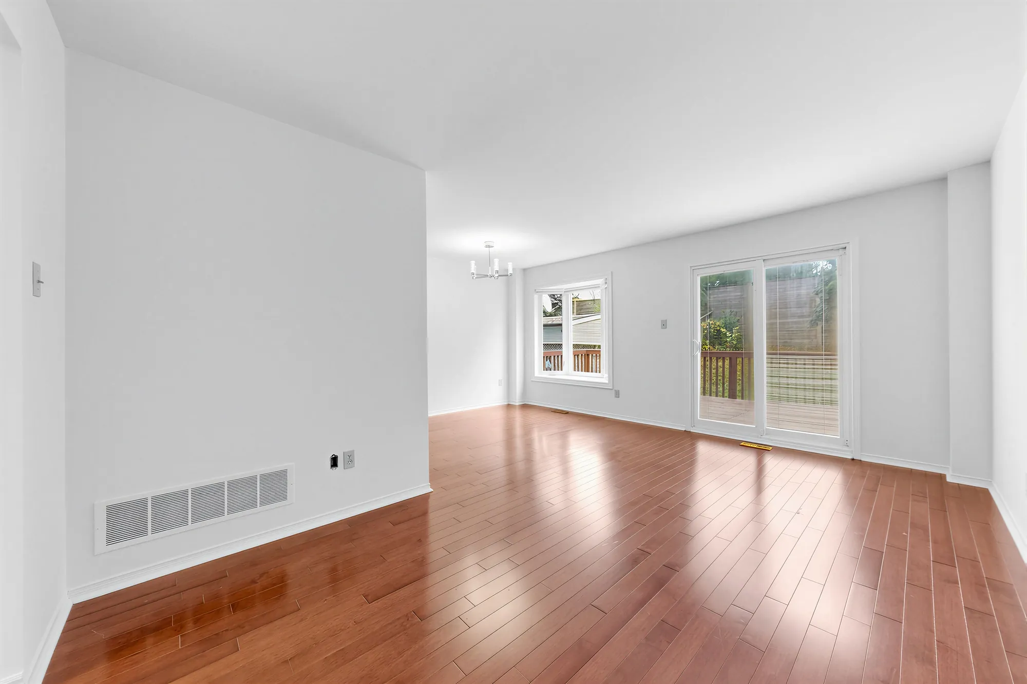 The living and dining room toward a window and the sliding door to the deck, a modern chandelier, hardwood floors