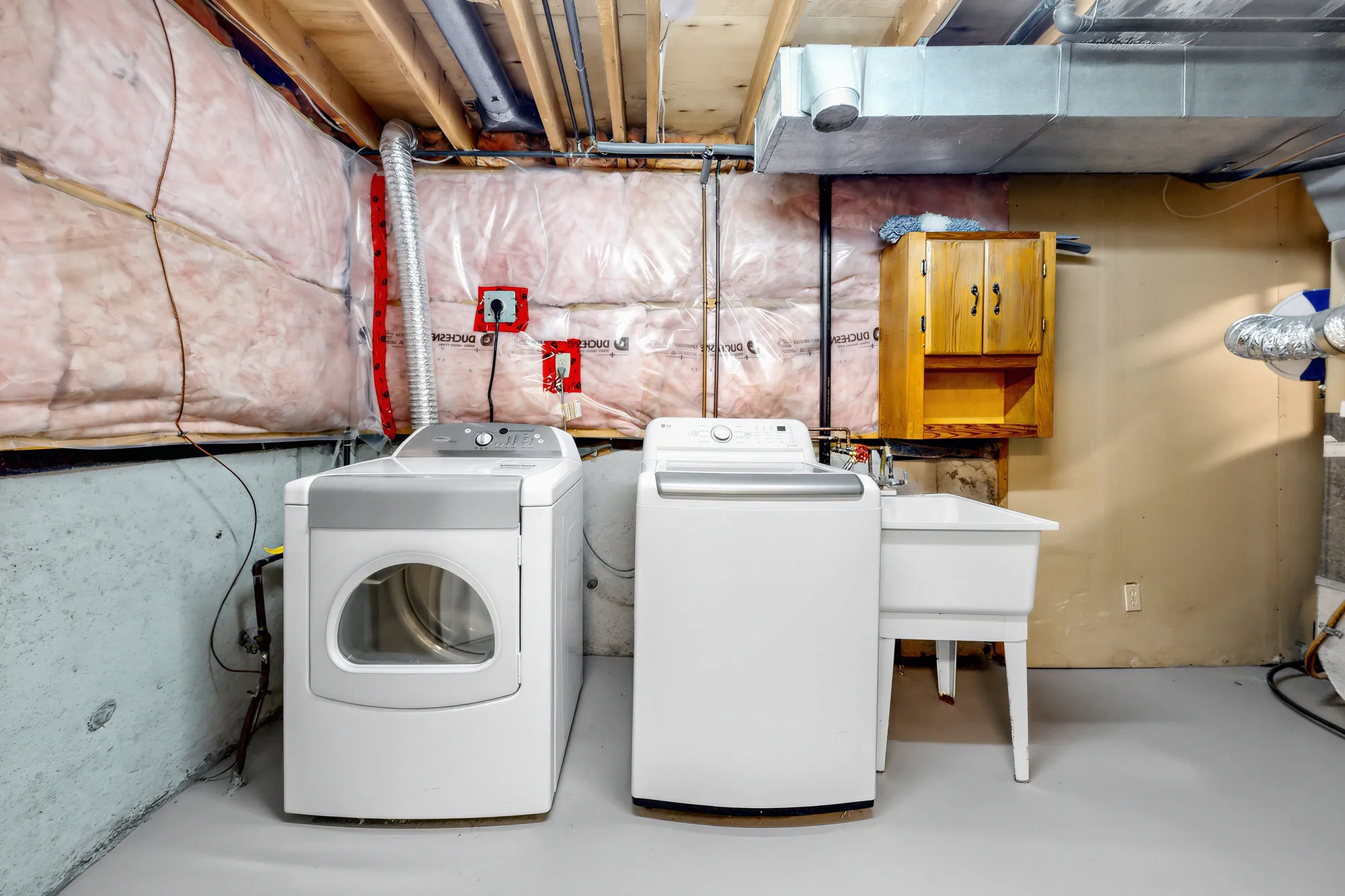 The utility room: a washer, a dryer and a laundry tub, insulated walls, ducts and pipes overhead, a cabinet on the wall