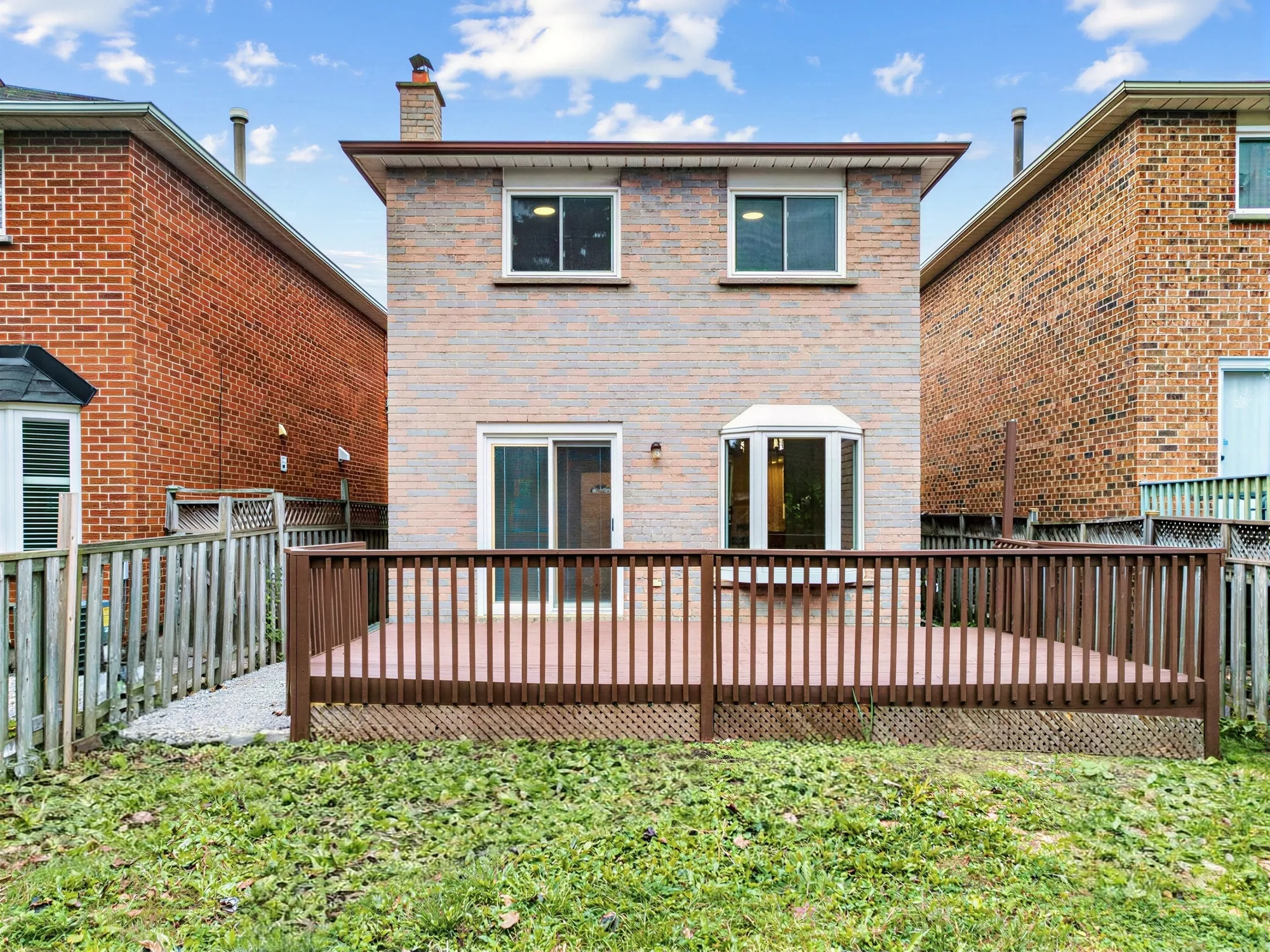 The back of the house from the yard: two storeys of brick, a sliding door and a bay window onto the deck with its wood railing, the lawn